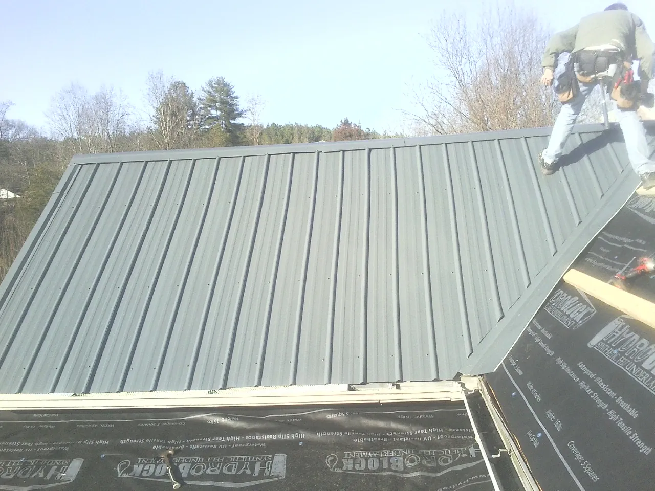 Crew installing dark green standing seam panels over synthetic underlayment in Lincroft
