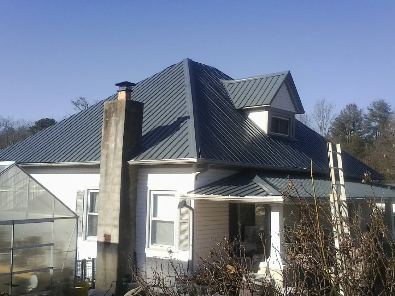 Dark blue standing seam metal roof on a white farmhouse with dormer — Slate & Tile Roof Repair by Roofing Brothers in Lincroft