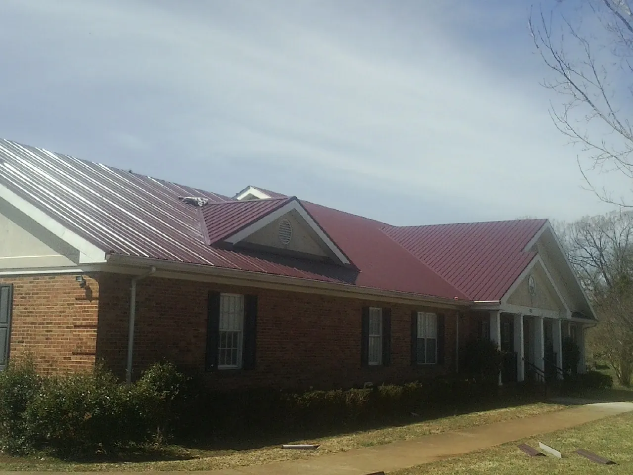 Red metal roof with gabled entries on a long brick building, from a Hail Damage Roof Repair job in Lincroft