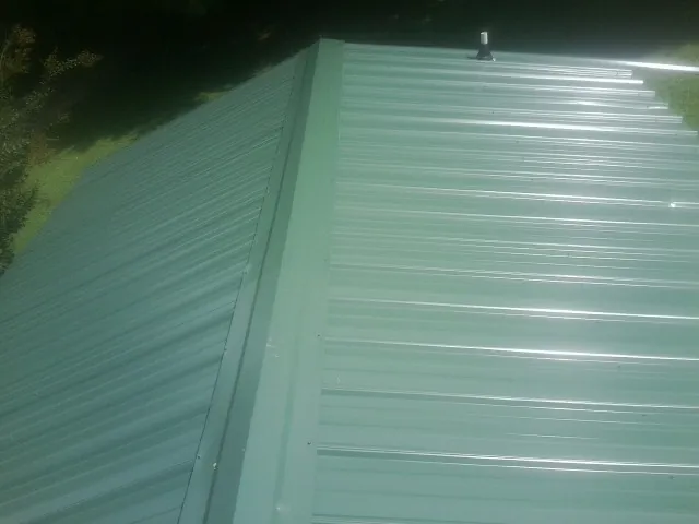 New green metal panels meeting at the ridge of a roof — Flat Roof Repair work by our crew in Lincroft