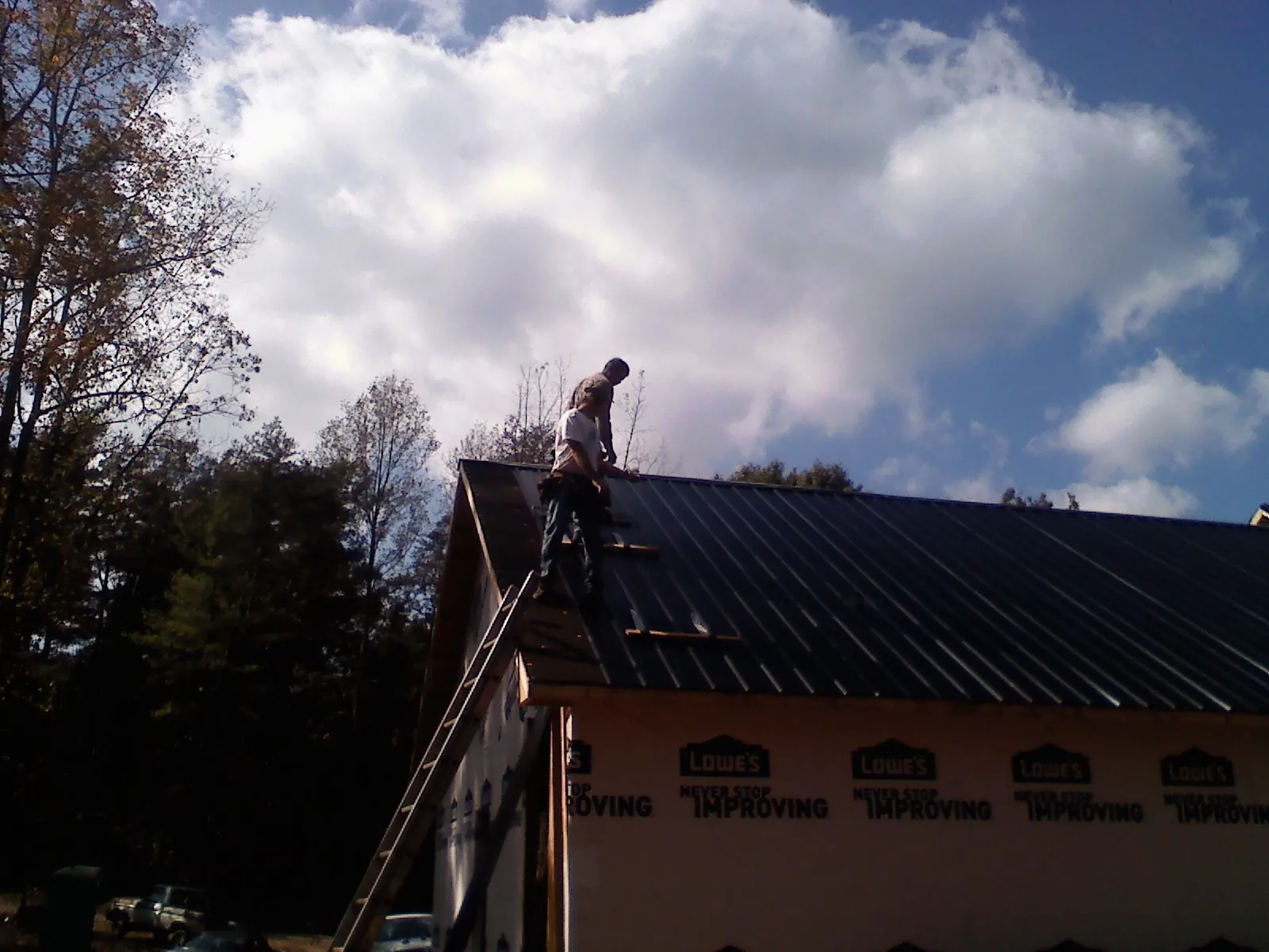 Roofer fastening dark metal panels high against a cloudy sky, from a Roof Inspection job in Lincroft