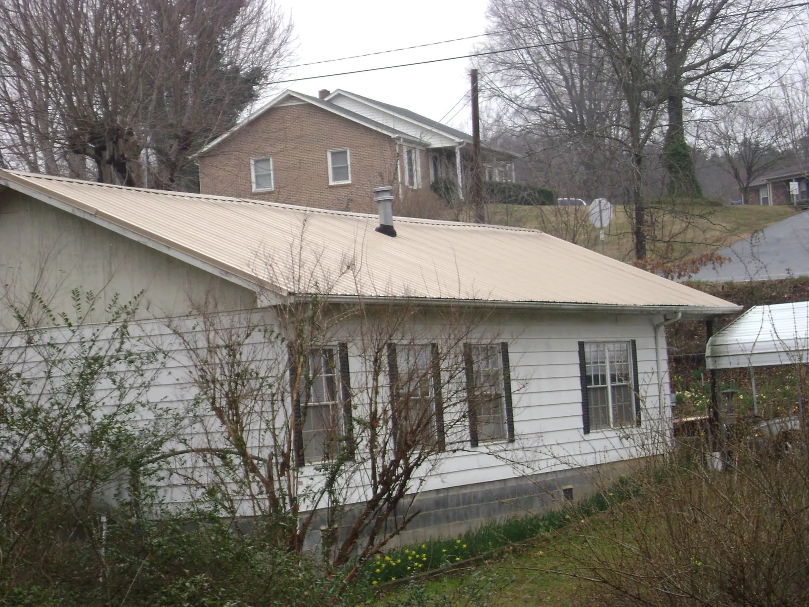 Tan metal roof on a white sided house set into a hillside — Commercial Roofing by Roofing Brothers in Lincroft